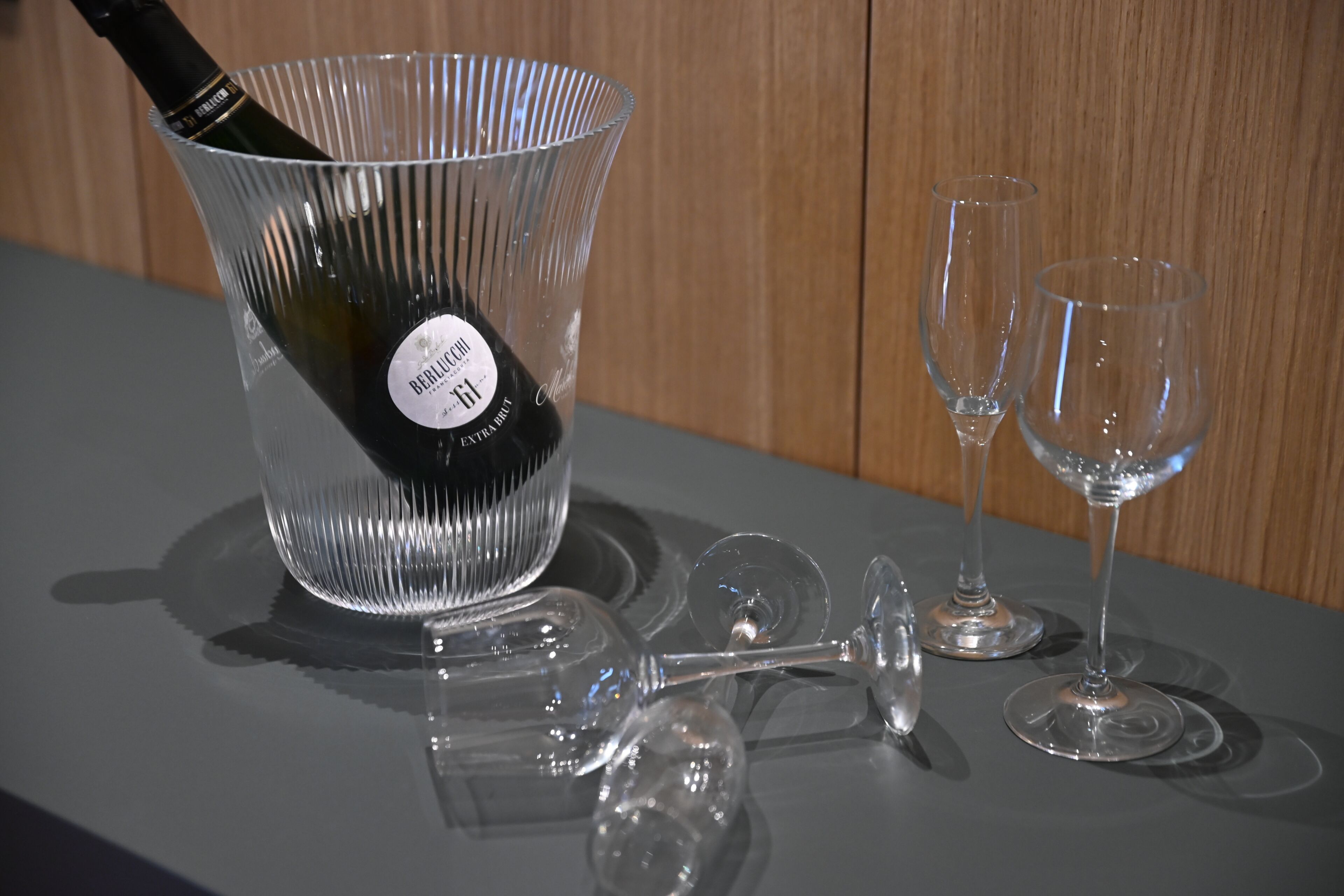 A bottle of wine in a glass container with two empty wine glasses on a table.