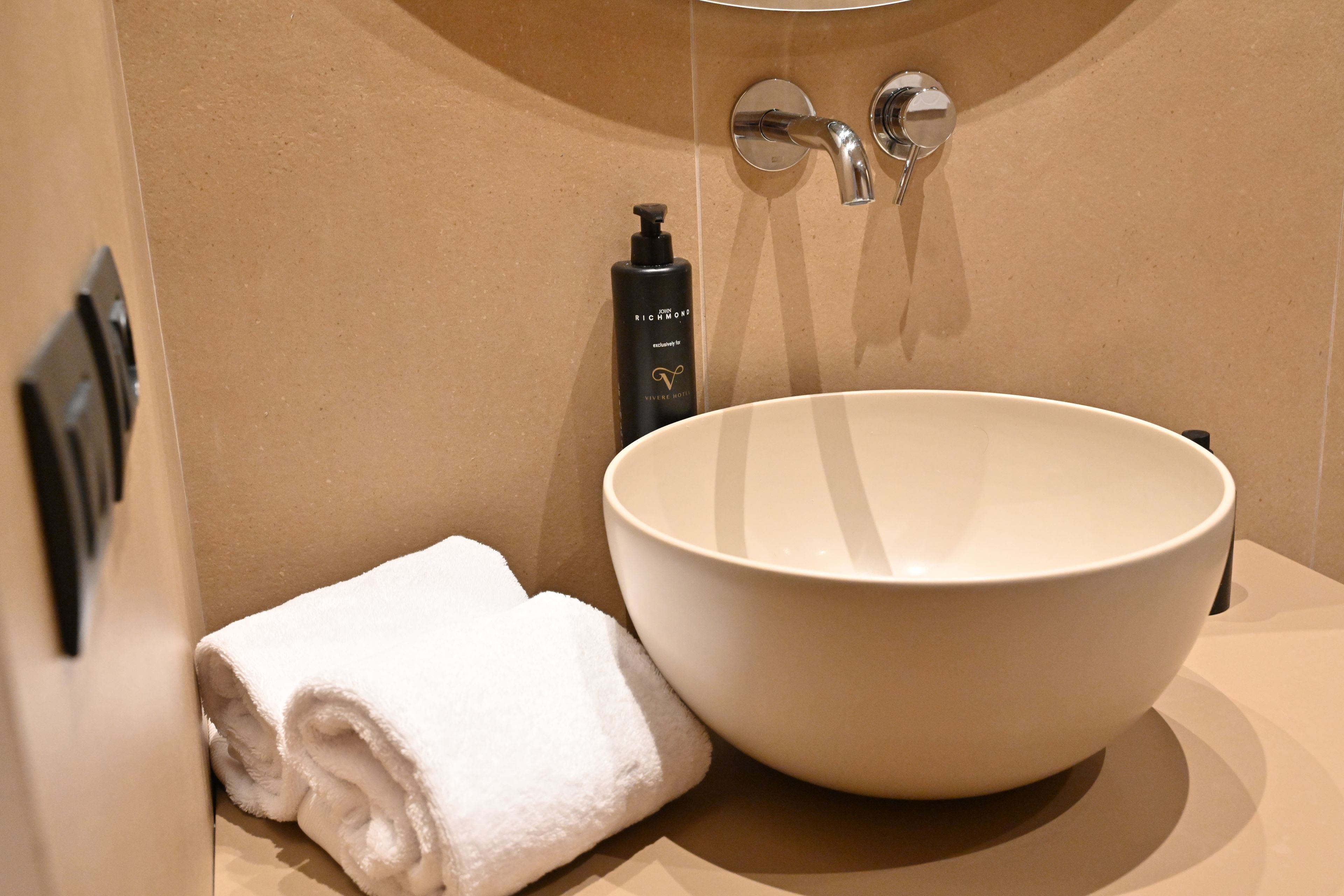 Un bagno con un lavandino bianco ampio, un asciugamano e una bottiglia di shampoo.