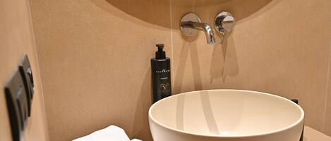 A bathroom with a large white basin, a towel, and a bottle of shampoo.