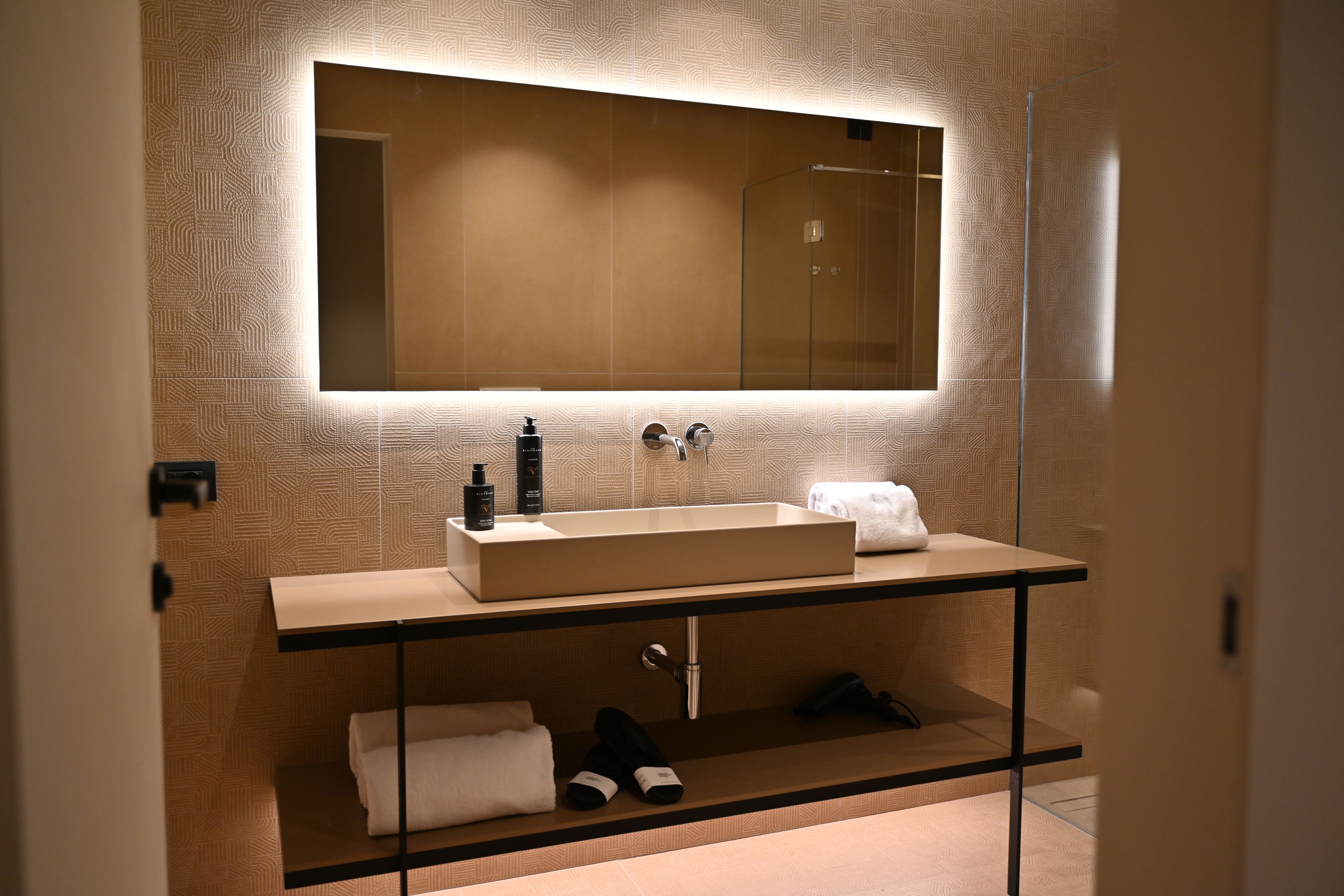 A modern bathroom with a large mirror, a rectangular sink, and a towel rack.