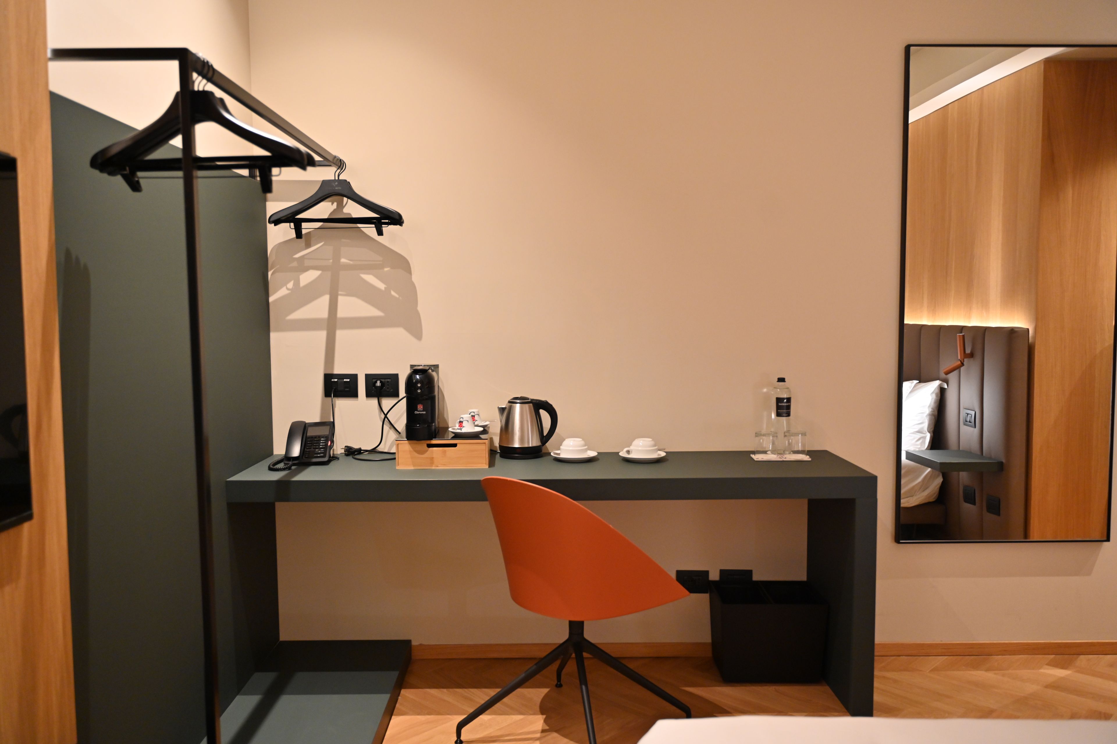 A hotel room with a desk, a chair, a telephone, a coffee maker, cups, and a water bottle.
