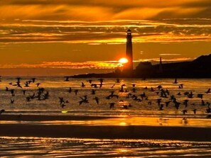 Un coucher de soleil sur une plage, avec un phare en arrière-plan.