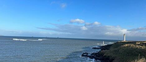 A coastal scene with a lighthouse, rocky shoreline, and ocean waves.