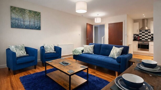 A modern living room with a blue sofa set, two armchairs, a coffee table, and a painting on the wall.