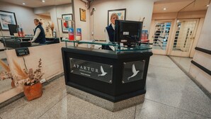 A reception desk with a glass partition, a sign reading 'APARTUR,' and a potted plant. - Apartur Buenos Aires (Buenos Aires)