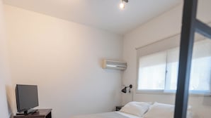A bedroom with a bed, a TV on a wooden stand, a window, and a wall-mounted air conditioner. - Apartur Buenos Aires (Buenos Aires)