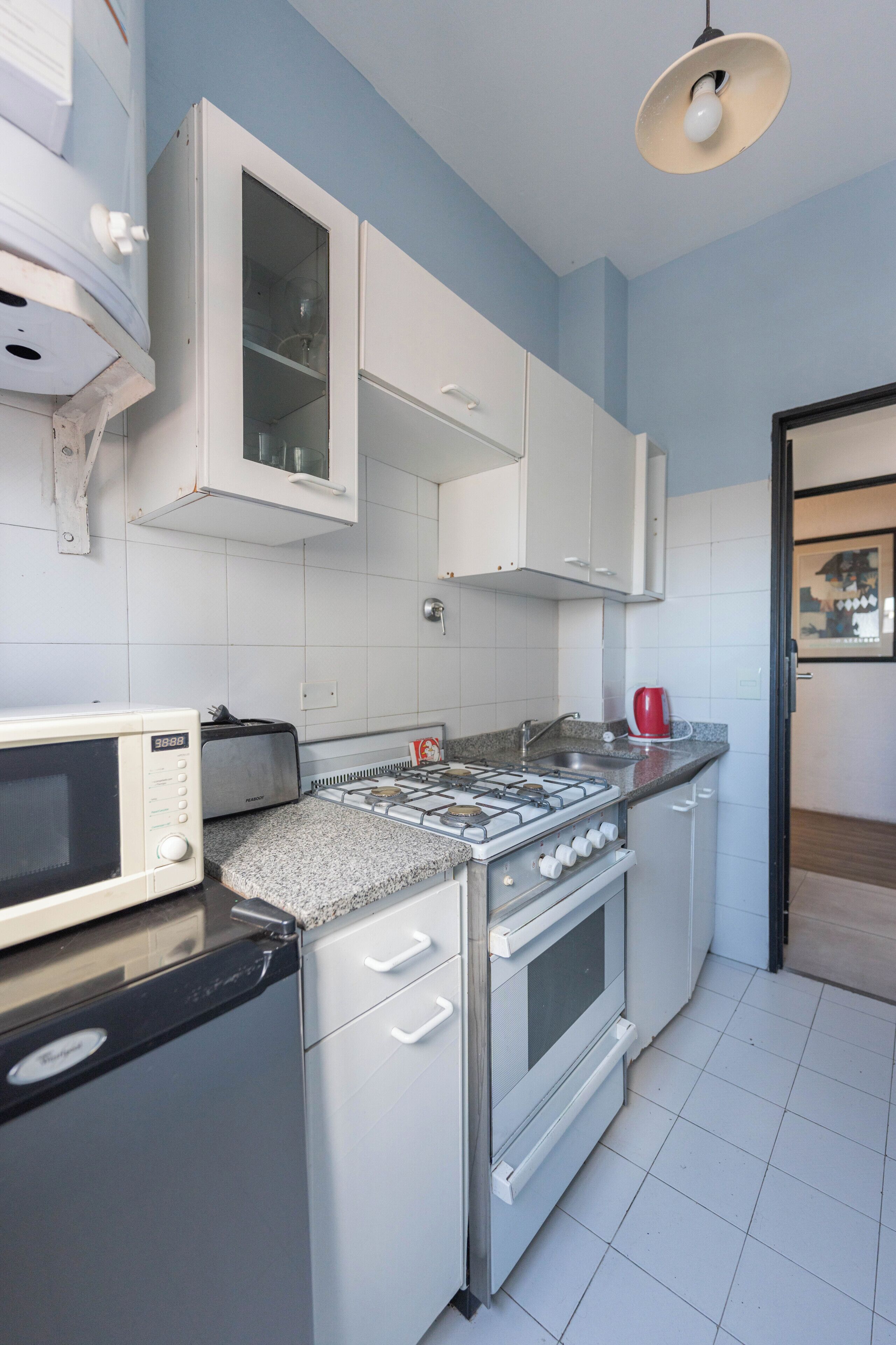 Una cocina compacta con armarios blancos, estufa a gas, microondas y tostadora.