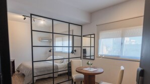A modern hotel room with a bed, a round table with chairs, a window with blinds, and a ceiling light fixture. - Apartur Buenos Aires (Buenos Aires)