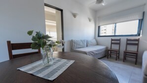 A dining table with a vase of flowers, a striped placemat, and a view of a living area with a sofa and chairs. - Apartur Buenos Aires (Buenos Aires)