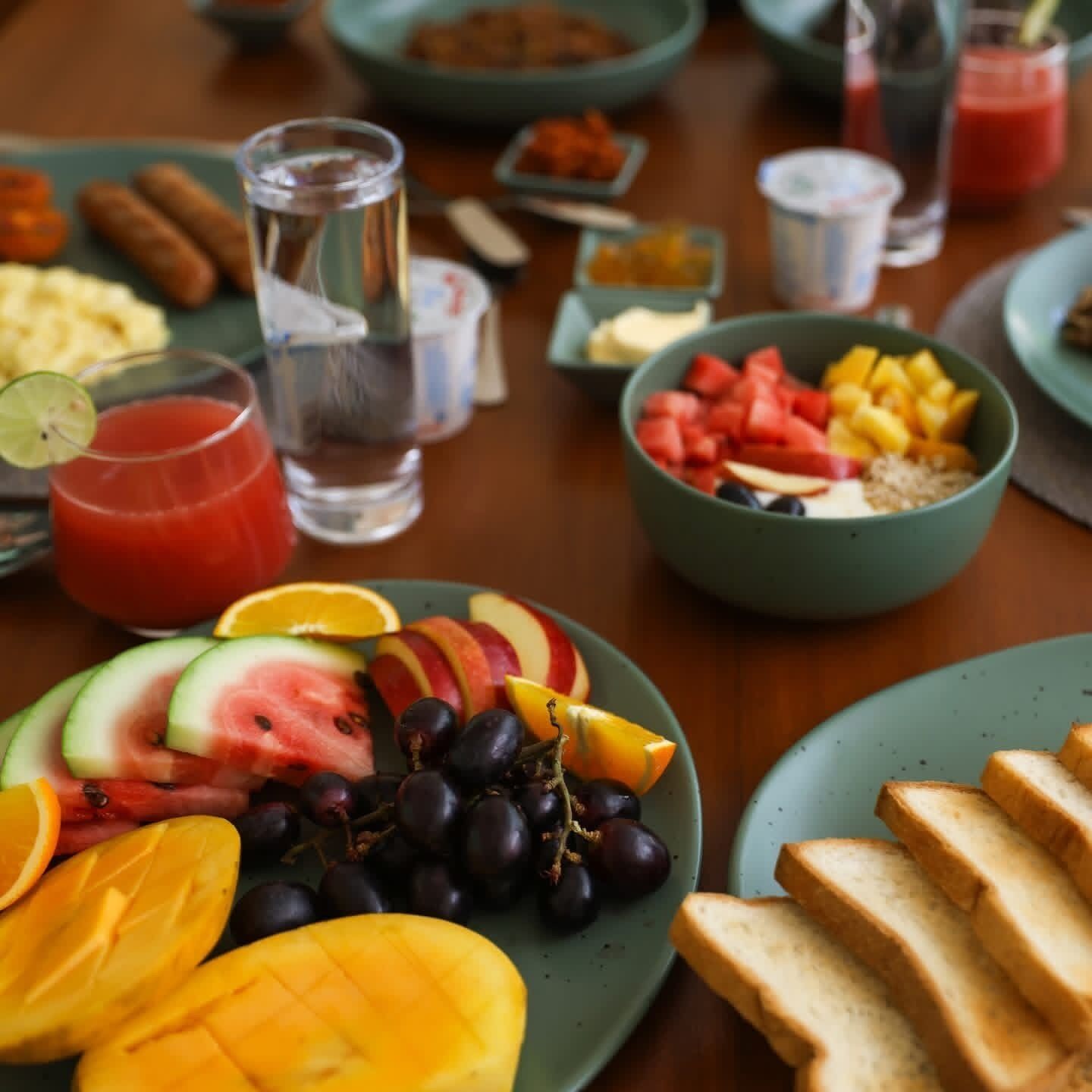 A breakfast setting with plates of fruit, toast, and a glass of juice.