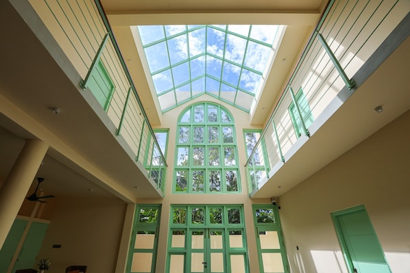 A high-ceiling atrium with a skylight, green-framed windows, and a central arched window.