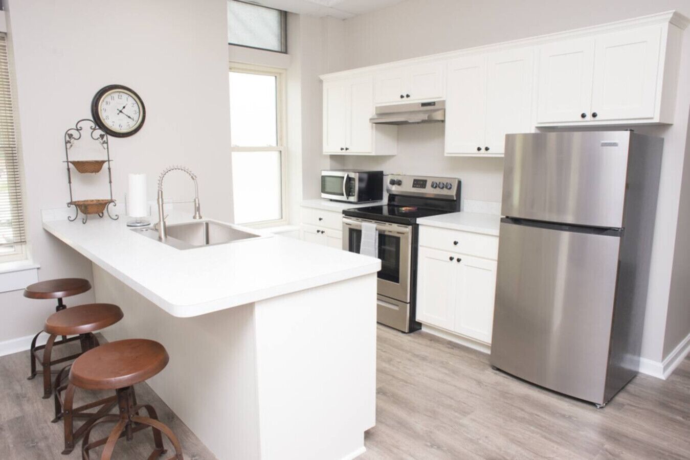A modern kitchen with white cabinetry, stainless steel appliances, a sink, and stools.