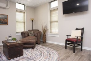 A living room with a brown leather sofa, a red chair, a round rug, a floor lamp, and a flat-screen TV mounted on the wall. - Downtown Millersburg, 2 Bedroom, 2 Bath Apartment (Millersburg)