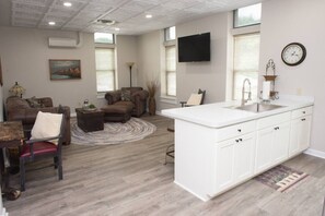 A spacious living area with a sofa, armchair, and a small dining table. A kitchen area with a white countertop and sink is visible. - Downtown Millersburg, 2 Bedroom, 2 Bath Apartment (Millersburg)