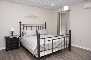 A bedroom with a metal-framed bed, a bedside table with a lamp, and a decorative wall piece. - Downtown Millersburg, 2 Bedroom, 2 Bath Apartment (Millersburg)