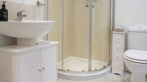 Un baño moderno con ducha de vidrio, lavamanos blanco y retrete.