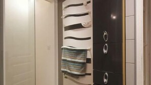 Een badkamer met een douchecabine van glas, een handdoekrek met gestreepte handdoeken, een zwart kastje met zilveren handgrepen en een blauwe prullenbak.