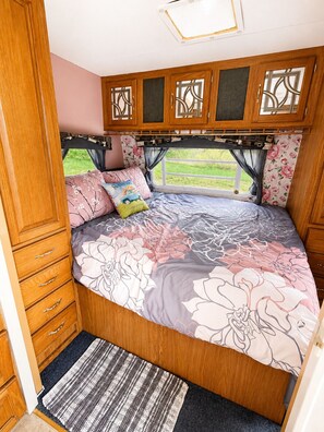 Un dormitorio con cama curva, armarios de madera, ventana con cortinas y vistas a la vegetación.