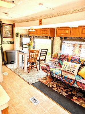 Interior compacto de una autocaravana con zona de comedor, kitchenette y un sofá colorido.