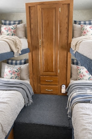 Un dormitorio con un armario de madera, dos camas con ropa de cama floral y una mesita de noche pequeña con una lámpara.