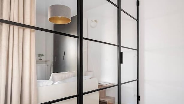 Quarto moderno com porta de vidro deslizante, piso de madeira em padrão herringbone e luminária pendente.
