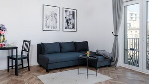 Uma sala de estar moderna com piso de madeira em padrão herringbone, um sofá azul escuro, uma mesinha lateral e um lustre.