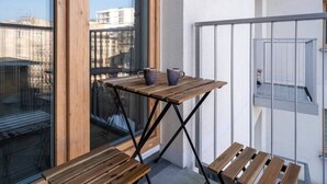 Uma varanda com mesa e banco de madeira, porta de vidro e vista para a cidade.