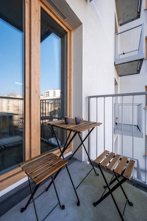A balcony with a wooden table and bench, a glass door, and a view of the cityscape. - Łódź Downtown - Balcony, Top Location- by Rentujemy (Łódź)