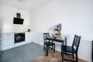 A modern kitchen with white cabinetry, a built-in oven, and a marble backsplash. There is a dining table with chairs and a vase of flowers. - Łódź Downtown - Balcony, Top Location- by Rentujemy (Łódź)