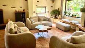 A living room with sofas, a coffee table, a bookshelf, and a window with plants. - Les étoiles (Mareugheol)