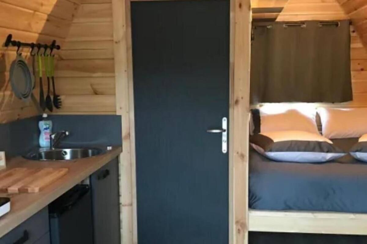 A compact wooden cabin with a kitchenette, a single bed, and a door leading to another room.