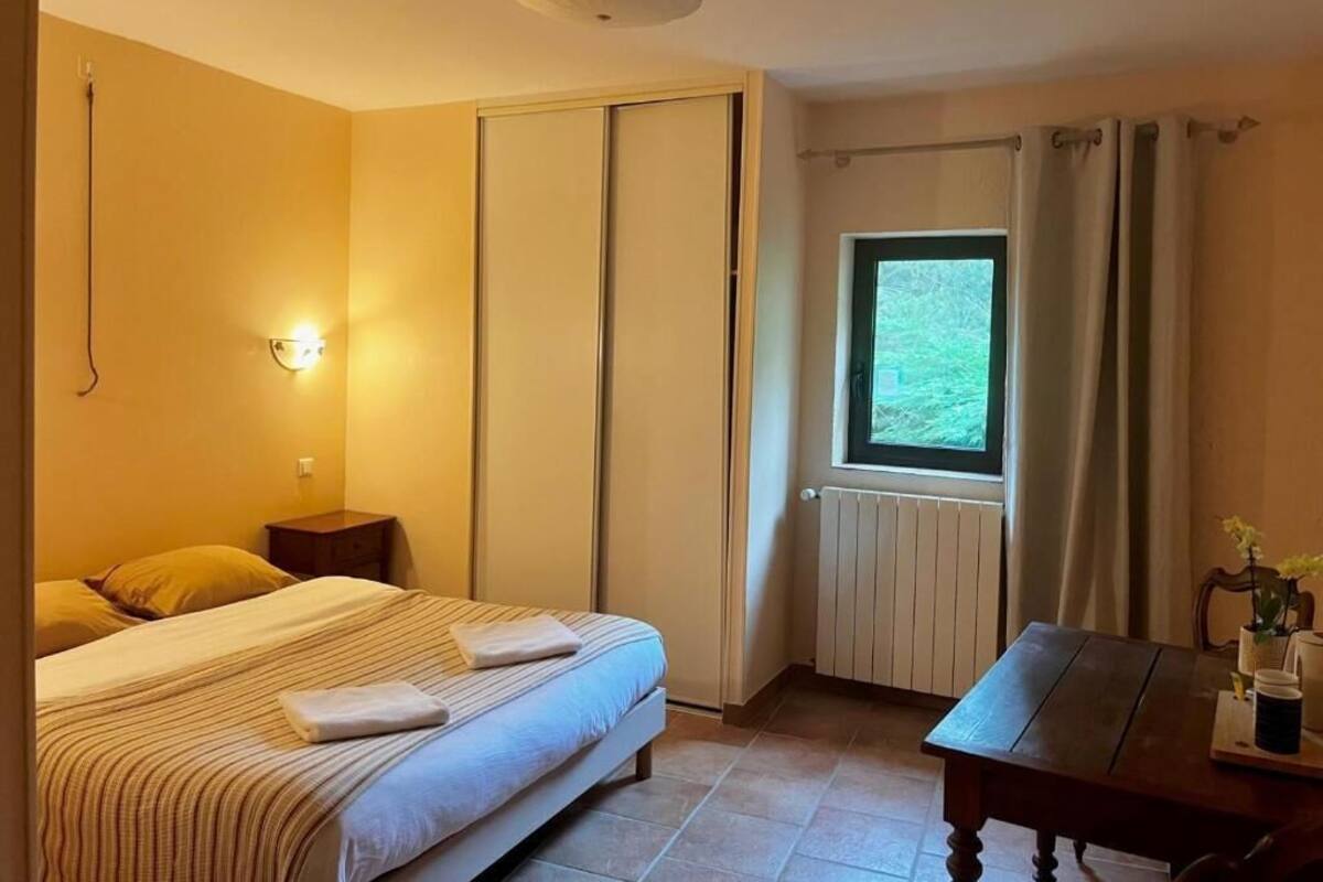 A bedroom with a bed, bedside table, window, and a view of greenery outside.