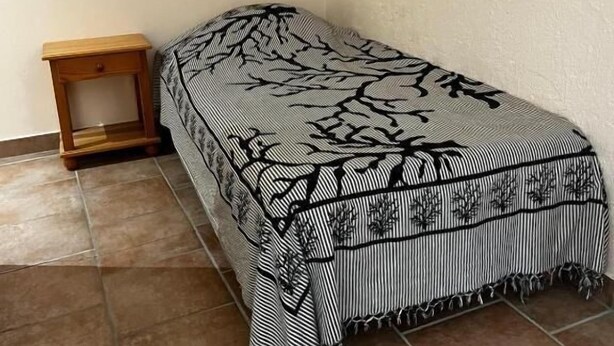 A single bed with a black and white patterned bedspread in a room with a tiled floor and a small wooden nightstand. - Les étoiles (Mareugheol)