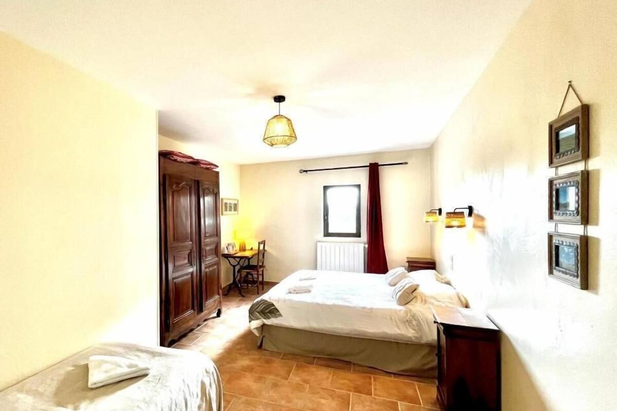 A bedroom with two beds, a wooden wardrobe, a desk with a chair, a hanging light fixture, and a window with curtains.