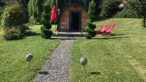 A small wooden cabin with a gravel path leading to it, surrounded by greenery and red chairs. - Les étoiles (Mareugheol)
