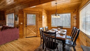 L’intérieur d’un chalet en bois comprend une table à manger pour quatre personnes, un canapé et une grande fenêtre équipée de stores.