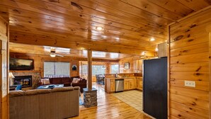 Un intérieur de chalet chaleureux avec une cheminée en pierre, un plancher en bois, un canapé et un coin cuisine.