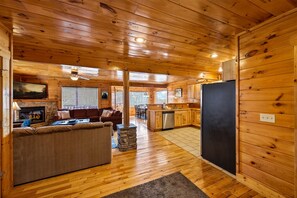 A cozy cabin interior with a stone fireplace, wooden floors, a sofa, and a kitchen area. - Perfect Cabin in Paradise: Hot Tub, Pool, Games! (Sevierville)