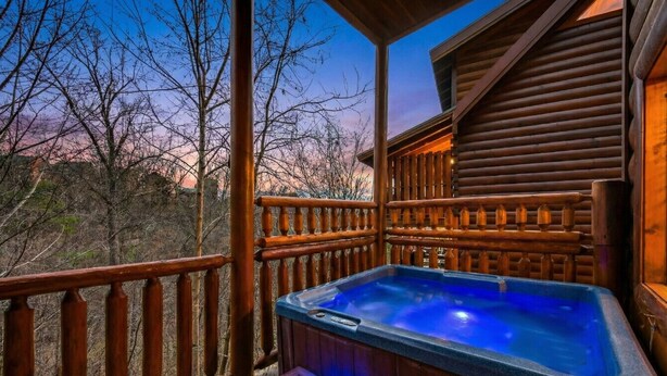 Un bain à remous en bois installé sur une terrasse dotée d’une rambarde en bois, entouré d’arbres et surplombant un ciel dégagé.