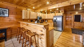 L’intérieur d’une cabane en bois comprend un espace cuisine avec des meubles de rangement en bois, un réfrigérateur en acier inoxydable et un bar avec des tabourets.