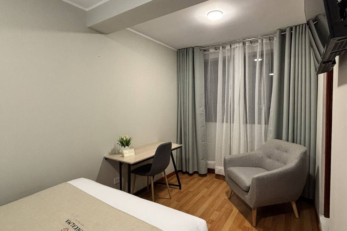 A hotel room with a bed, a desk, a chair, and a window with curtains.