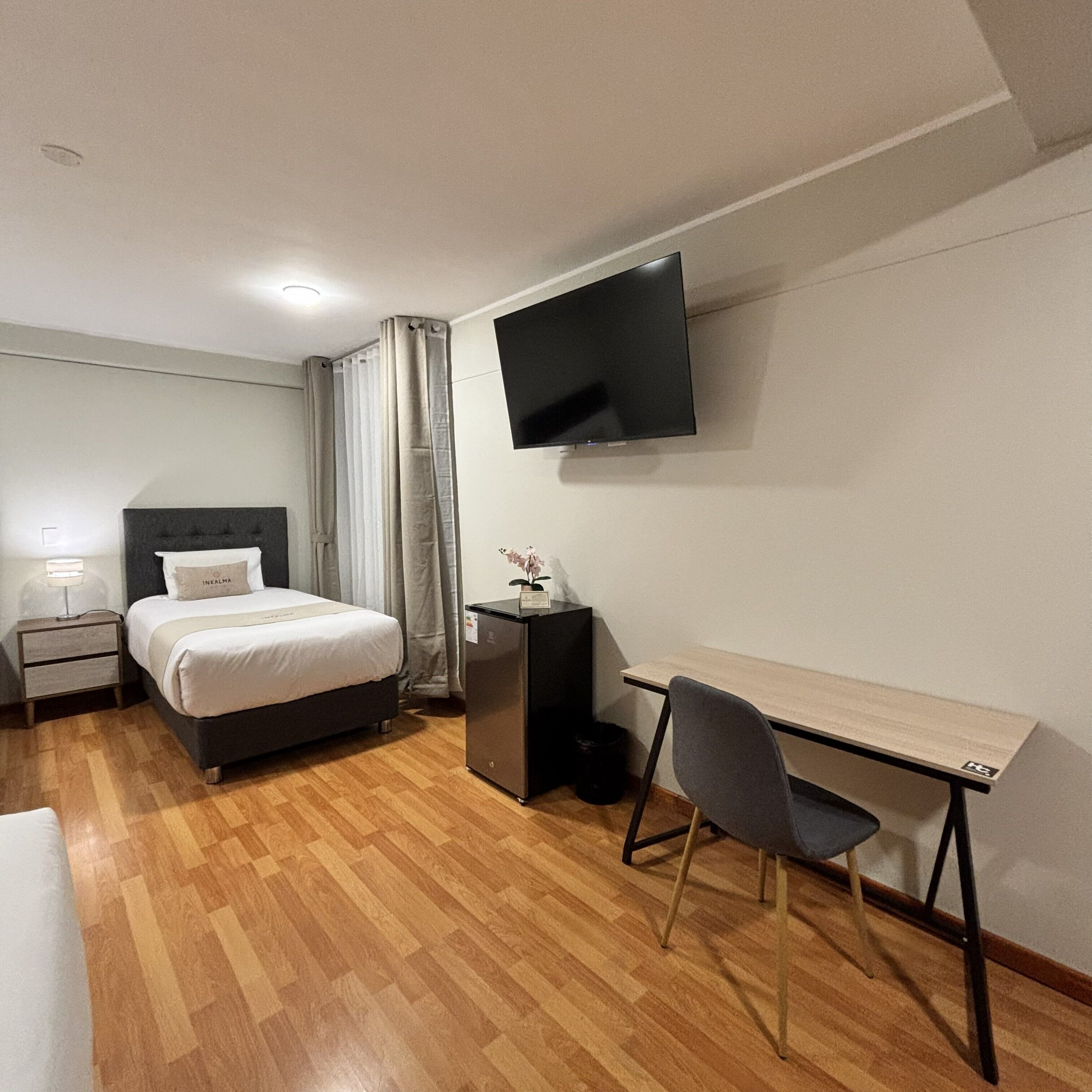 Una habitación de hotel con cama, escritorio, silla, televisor y mesita de noche.