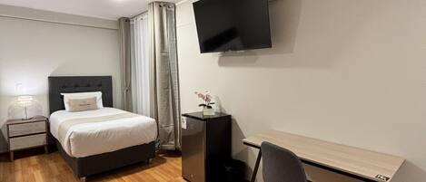 Una habitación de hotel con cama, escritorio, silla, televisor y mesita de noche.
