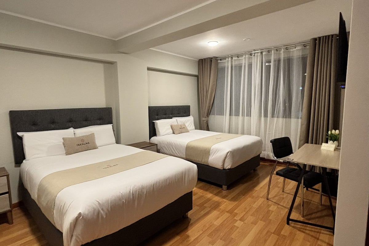 A hotel room with two beds, a small table, a chair, and a TV.