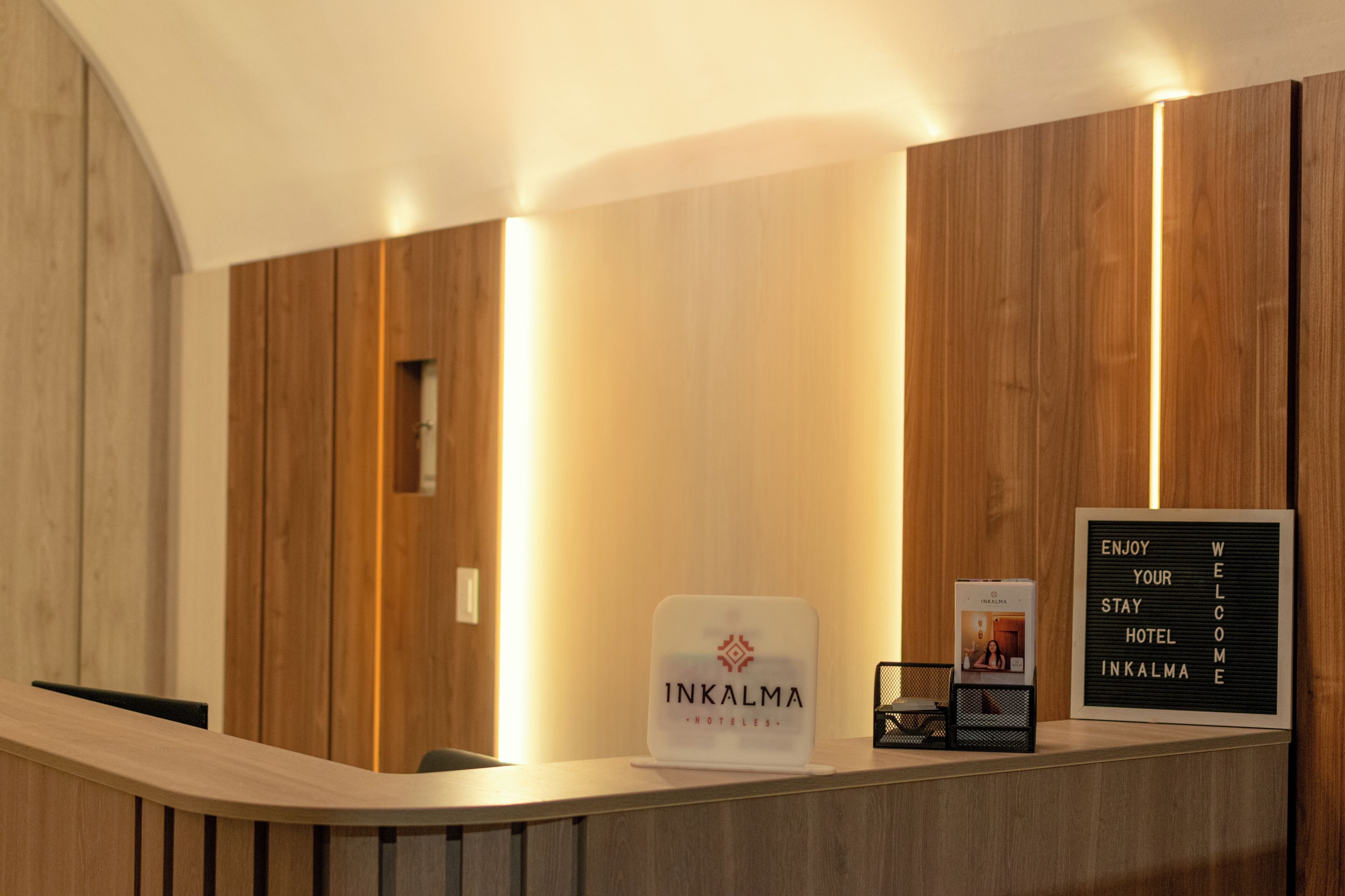 Ein Empfangsbereich mit einem Schild, das 'INKALMA HOTELS' zeigt, einem gerahmten Willkommensschild und einer Kaffeemaschine.