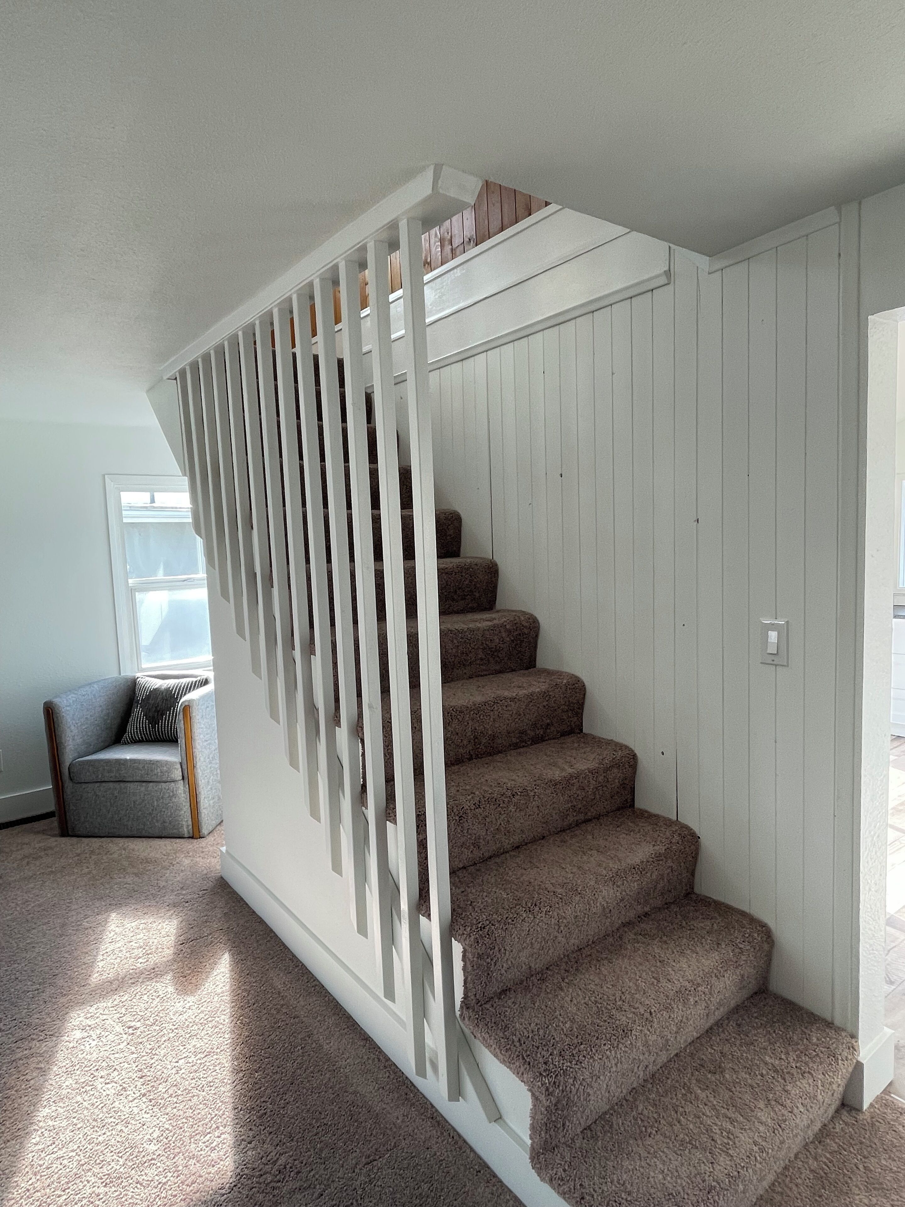 A staircase with white railings and carpeted steps in a room with a window and a chair.
