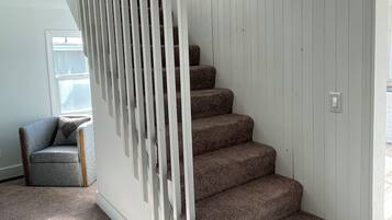 A staircase with white railings and carpeted steps in a room with a window and a chair.