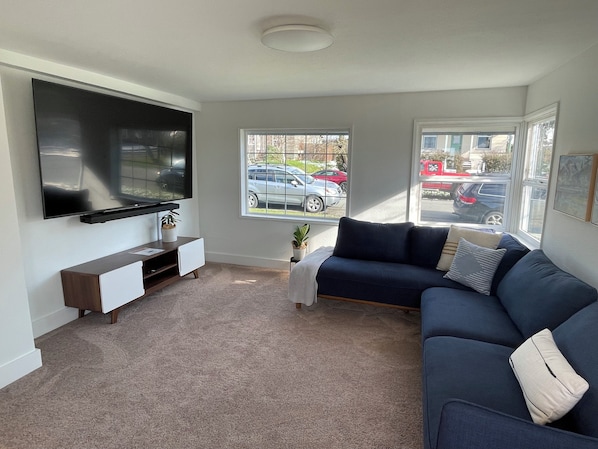 A living room with a flat-screen TV, a dark blue sofa, a white cabinet, and a small side table with a plant.