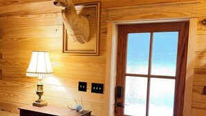 En inredning med träpaneler och ett rådjurshuvud som hänger på väggen, en trädörr med frostade glaspaneler, en lampa på en byrå och eluttag på väggen.