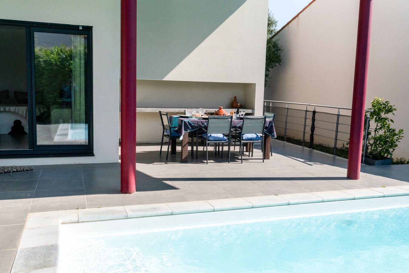A poolside area with a table and chairs, a glass door, and a red pillar.